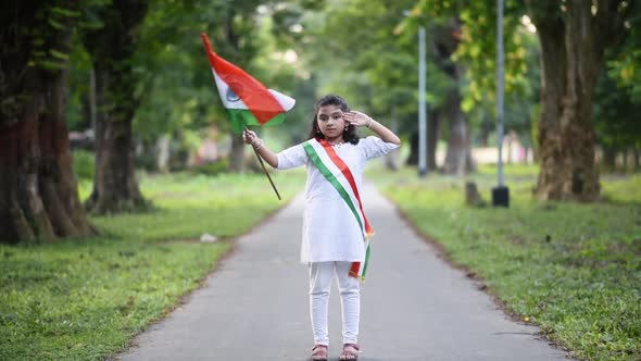 A cute little Indian girl is waving Indian tricolor flag in slow motion and salutes to the camera