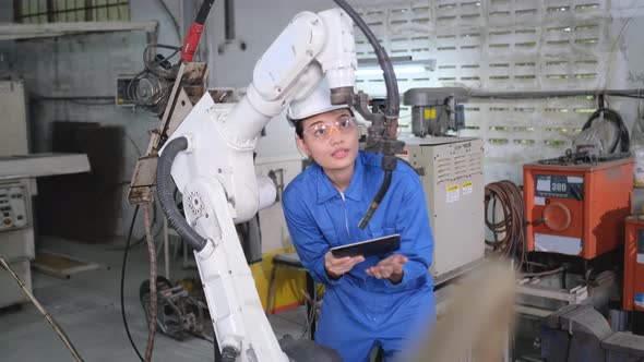 Factory worker woman or technician hold laptop and inspect function of industrial robot machine