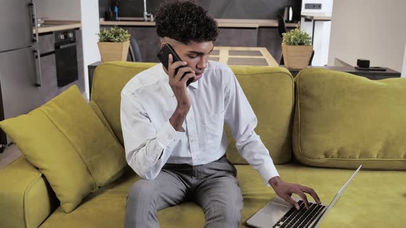 Close-up Young Afro Man Using Laptop Computer and Makes Phone Calling in Home Office