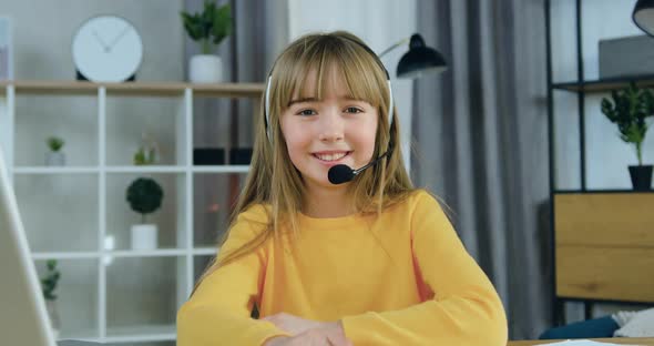 Girl in Headset Dressed in Casual Clothes Sitting in front Camera on the Background