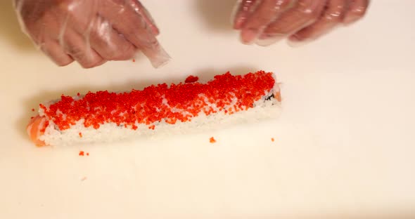 Chef Wearing Gloves Puts Red Caviars On Top Of Sushi Roll. - high angle shot