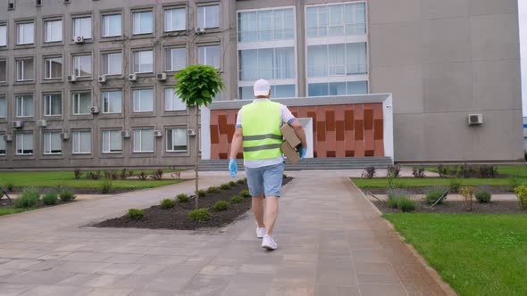 Male Courier, in Protective Mask, Gloves, Goes Through Courtyard of Hospital or Medical Facility