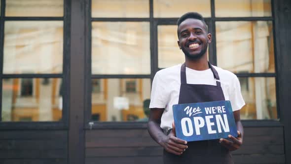 Slow Motion Portrait of African American Guy Urban Cafe Owner Posing with We Are Open Sign Standing