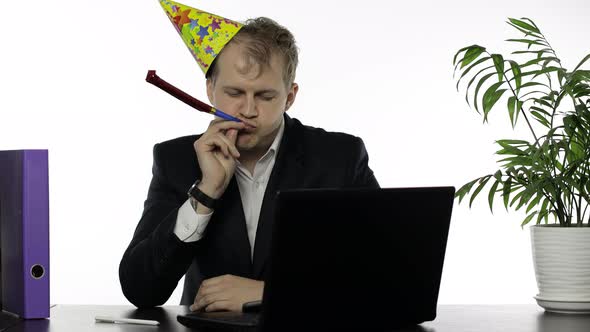 Drunk Sleepy Young Businessman in Festive Cap Blowing a Whistle. Hangover