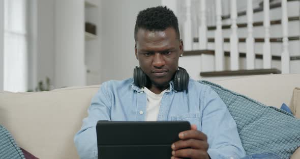 Young Confident Black Guy in Casual Clothes which Working on Tablet PC at Home