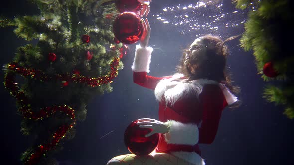 Happy Sexy Woman Is Holding Red Shiny Balls for Christmas Tree, Sitting Underwater