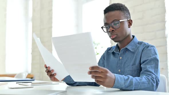 Focused Young African Man Reading Documents in Office