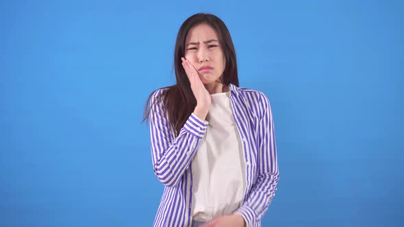 Beautiful Young Asian Woman Has a Toothache on a Blue Background