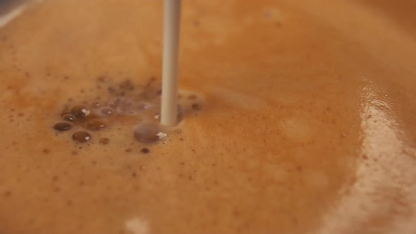 Slow motion shot of pouring milk into a frothy strong espresso 