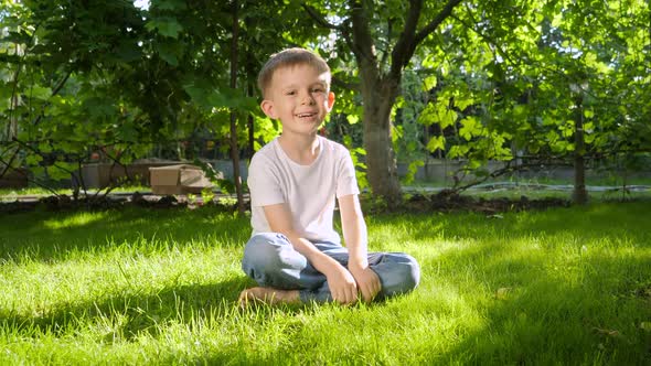 Dolly Shot of Happy Laughing and Smiling Boy Relaxing on Grass in Backyard Garden