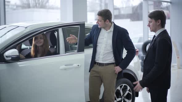 Happy Caucasian Young Woman Sitting in Car As Her Husband Talking with Dealer