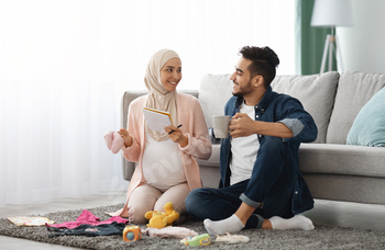 Happy pregnant muslim couple getting geady for childbirth, making checklist at home