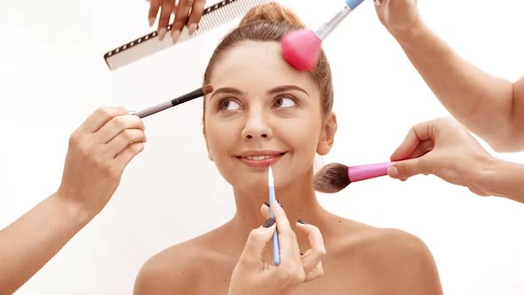 Hands Doing Hairstyle and Make Up for Young Beautiful Naked Girl in Towel Over White Background