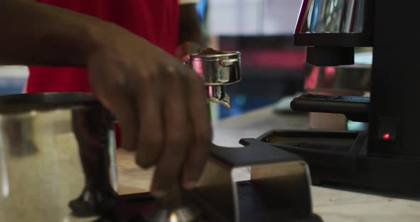 Midsection of african american male barista making coffee in coffee machine