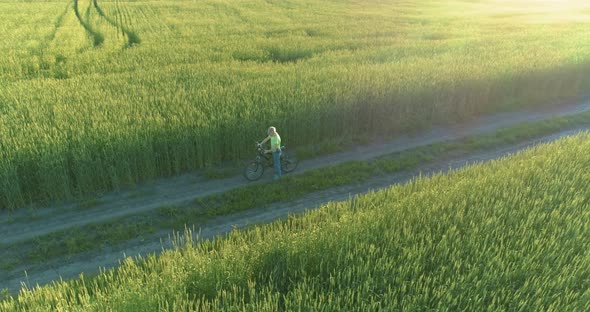 Aerial View on Young Boy, That Rides a Bicycle Thru a Wheat Grass Field on the Old Rural Road