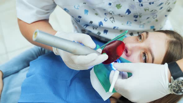 Dentist in white latex gloves uses a UV lamp with a red protective glass to solidify a dental