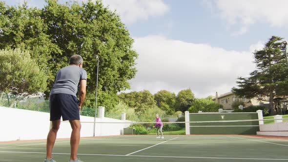 Video of biracial senior man playing tennis on tennis court