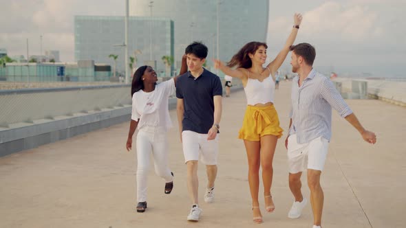 Happy Young Multiracial Best Friends Jumping and Having Fun While Walking Along Bridge on Summer Day