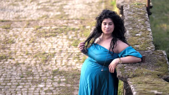 pregnant woman leaning against a wall arranges her hair smiling at camera