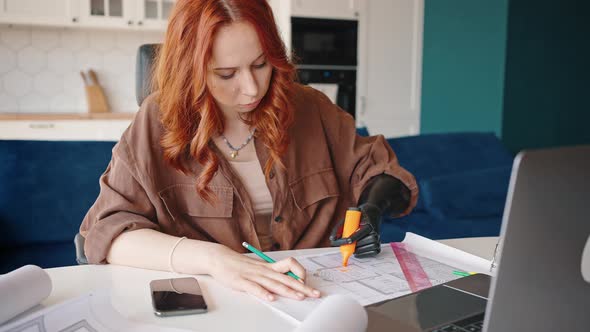 Redhaired Attractive Girl Designer with a Prosthetic Limb is Working on a Project in Her Home Office