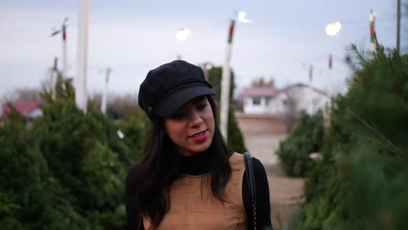 A hispanic woman shopping for a season holiday Christmas tree on a lot with many species of fir tree