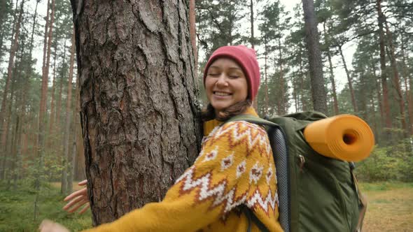 Lady in Yellow Sweater and Red Hat Hugs Old Pine in Forest