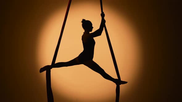 Silhouette of a Young Woman Performs Acrobatic Elements and Twine on Airy Silk