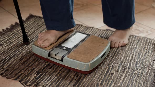 Senior sick woman stands on an old dirty scale and measures her weight.