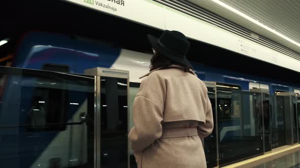Rear View of a Young Girl in a Hat Standing Next to a Passing Subway Waiting for a Ride