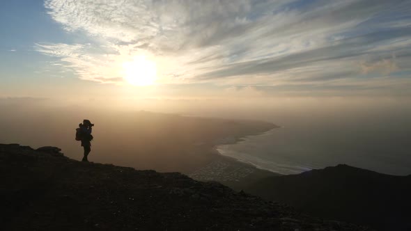 Silhouette of a Woman in Bicycle Helmet with Backpack Taking Pictures