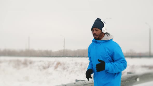 Black Man at Jacket and Headphones is Jogging in Winter Side View