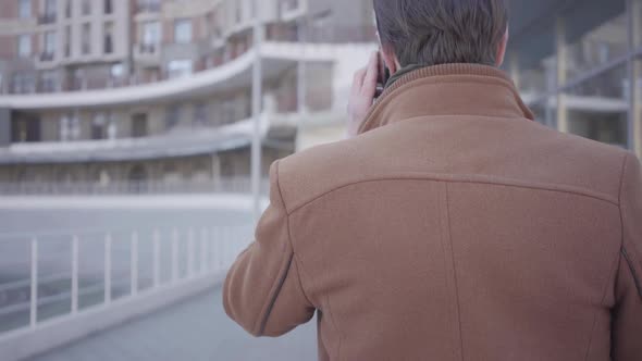 Back View of Handsome Successful Man in Brown Coat Walking on the City Street Talking By Mobile