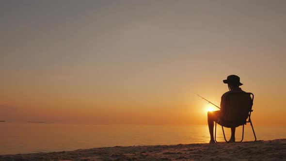 Silhouette of a Man Sitting By the Sea and Fishing.