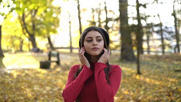 Brunette in a Cap Posing at Camera and Caressing Her Face in Sunny Autumn Park