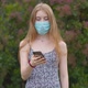 A young girl in a protective medical mask looks at the phone and sends messages - VideoHive Item for Sale