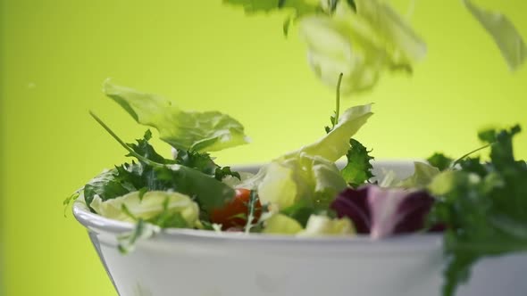 Fresh salad falling into bowl on green background