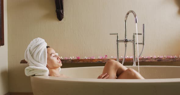 Relaxed biracial woman lying in bathtube and pampering herself with rose petals