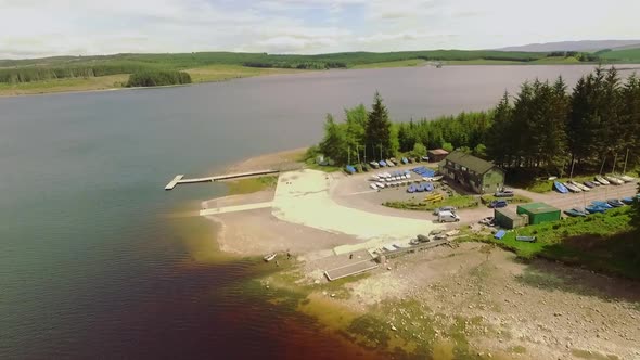 Flyover view of lake boathouse and boats moored at side of lake,