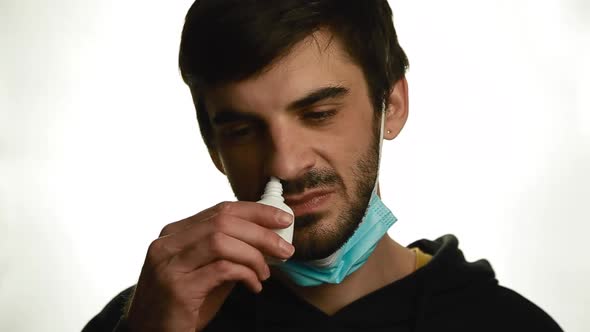 A Portrait of a Young Man Takes Off the Medical Mask and Sprays the Spray in the Nose in a White