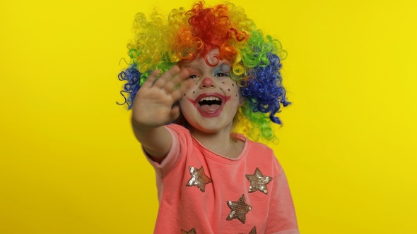 Little Child Girl Clown in Colorful Wig Waving Hands, Having Fun, Smiling. Halloween