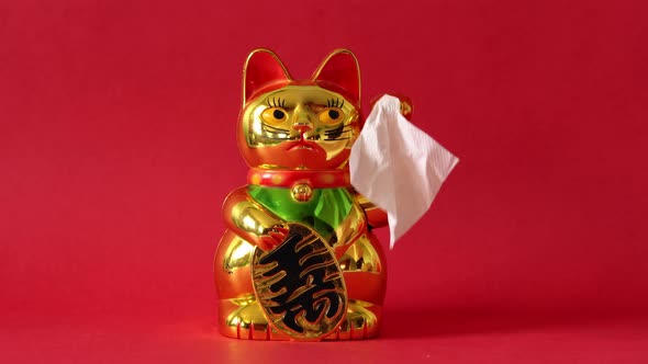 Golden Maneki-neko cat waving goodbye with tissue