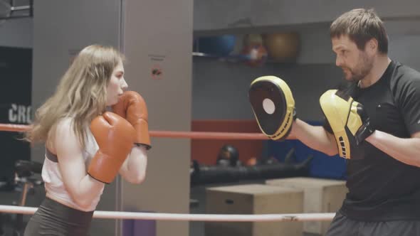 Sparring of Cheerful Female Boxer with Coach in Training Gloves on Ring. Side View Portrait of