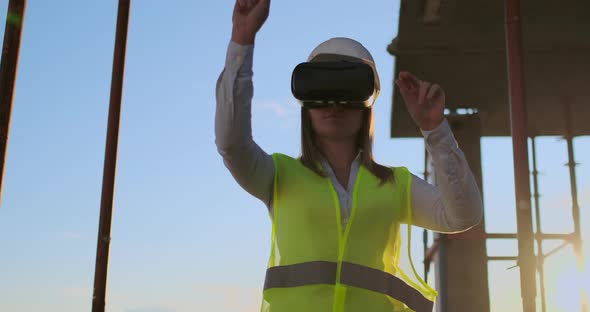 Woman Inspector in VR Glasses and Helmet Checks the Progress of the Construction of a Skyscraper