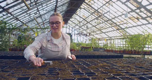 A Young Woman in Eyeglasses Loosens the Soil in the Cells After Planting the Seeds