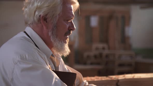 Portrait of an Old Experienced Carpenter checks the Perfection of the Wood Product.