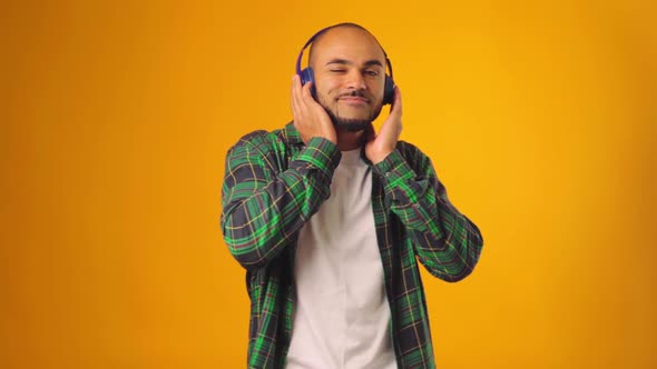Handsome Joyful African American Man Listening to Music with Headphones Against Yellow Background