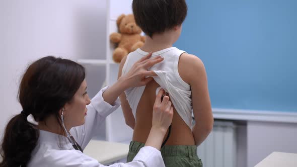 Back View Little Caucasian Boy Standing in Hospital As Doctor Using Stethoscope Listening to