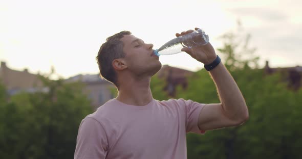 Medium Shot of Thirsty Young Man Drinking Water in Plastic Bottle Outdoors