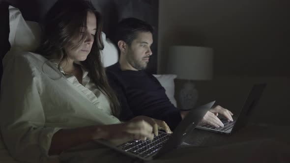 Young Couple Using Laptops in Bed