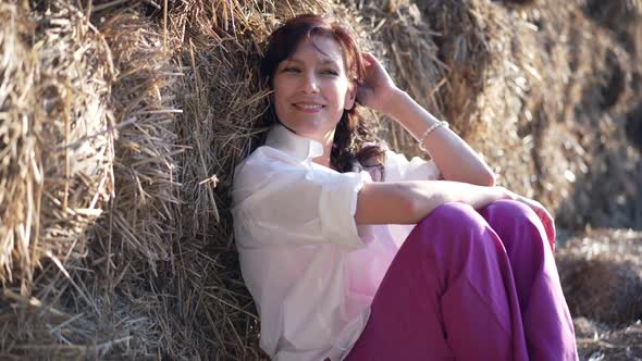 Beautiful Woman Dreaming Leaning on Hay Bale in Sunshine Outdoors Looking Away in Slow Motion
